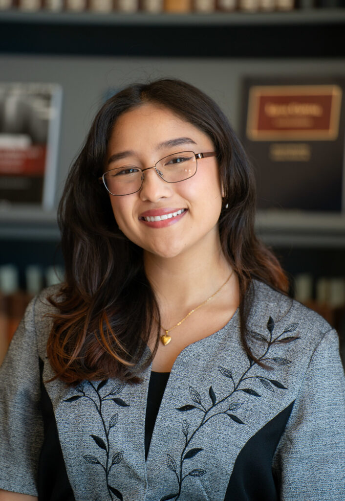 Smiling warmly, Jaeda stands in front of an office bookshelf filled with law books and awards.